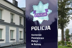 Podświetlana tablica, na której jest napis: Komenda Powiatowa Policji w Kolnie oraz policyjna gwiazda. T tle budynek KPP w Kolnie