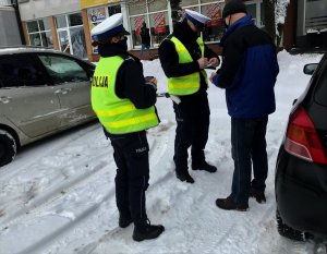 Dwóch policjantów wydziału ruchu drogowego legitymuje na parkingu mężczyznę.