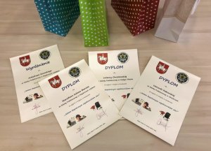 Cztery dyplomy dla laureatów konkursu Jestem bezpiecznym użytkownikiem sieci. Na nimi cztery torby prezentowe w kolorze niebieskim, zielonym i czerwonym w białe kropki oraz jedna w kolorze beżowym.