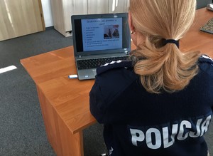 Policjantka siedzi przy stoliku, na którym stoi laptop.