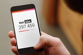 Telefon komórkowy trzymany w dłoni. Na jego ekranie napis: KOD BLIK i numer 297 459.