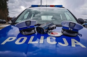 Czapki policjantów ruchu drogowego, tarcza do zatrzymywania pojazdów i miernik prędkości na masce policyjnego radiowozu.
