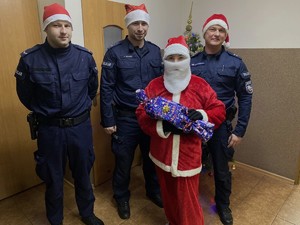 Policjanci w czapkach Mikołaja i Mikołaj z prezentem