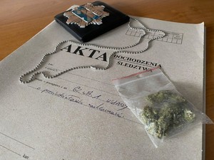 Marihuana w foliowym woreczku i policyjna odznaka leżące na aktach dochodzenia/śledztwa